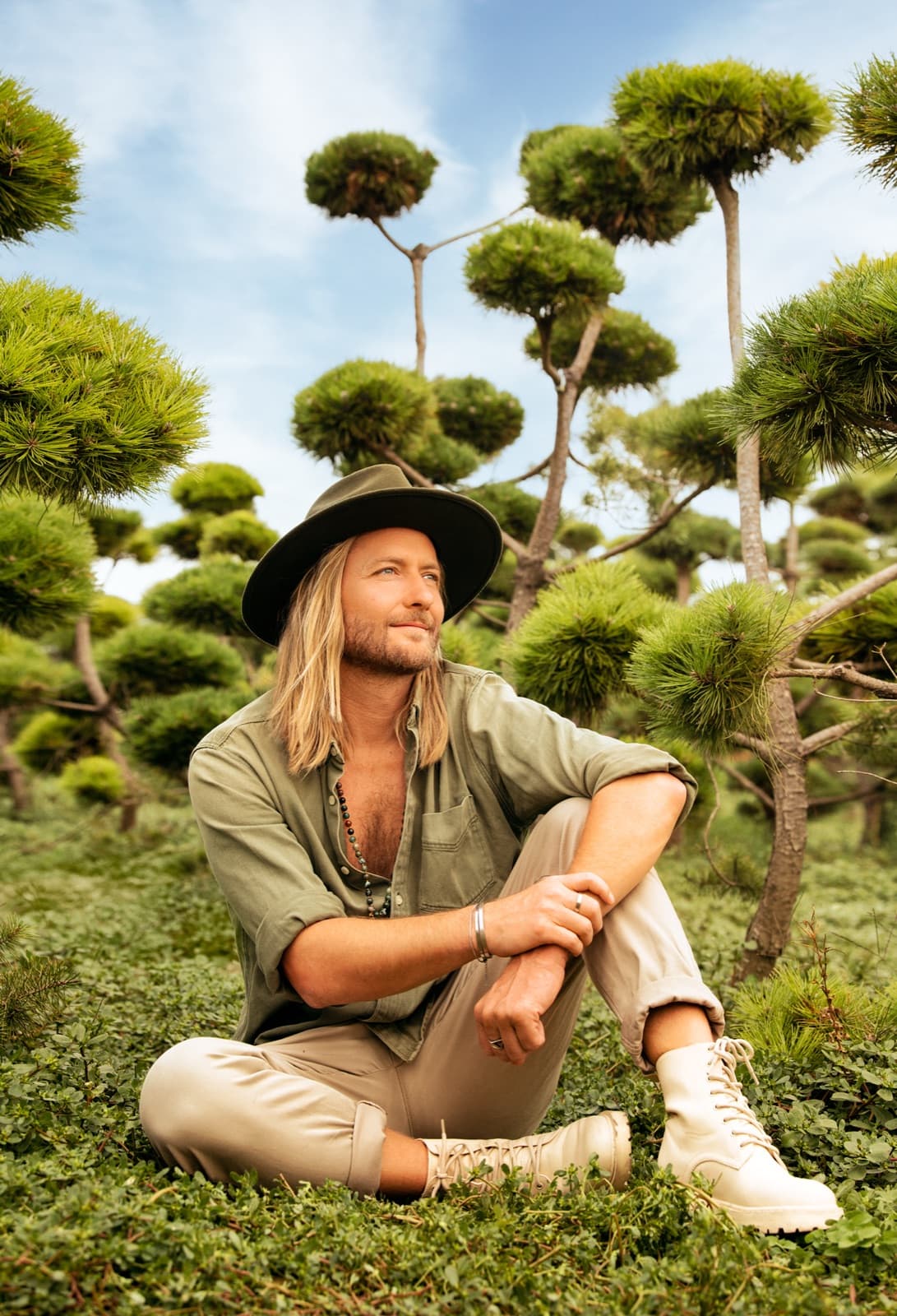 Victor Mathys seated among sculpted pines, wearing a wide-brimmed hat