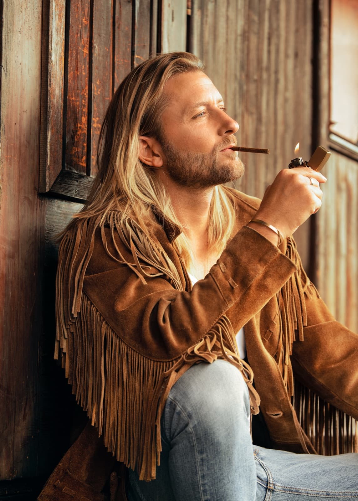 Victor Mathys in a fringed suede jacket against weathered timber, warm light
